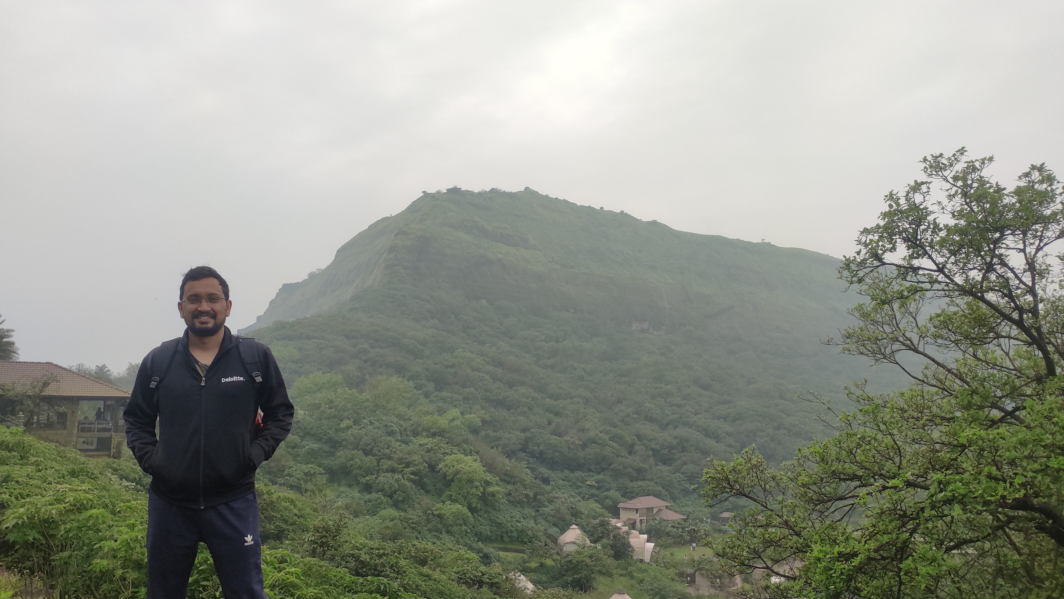 Tanmay in a Deloitte jacket standing in front of a green hill